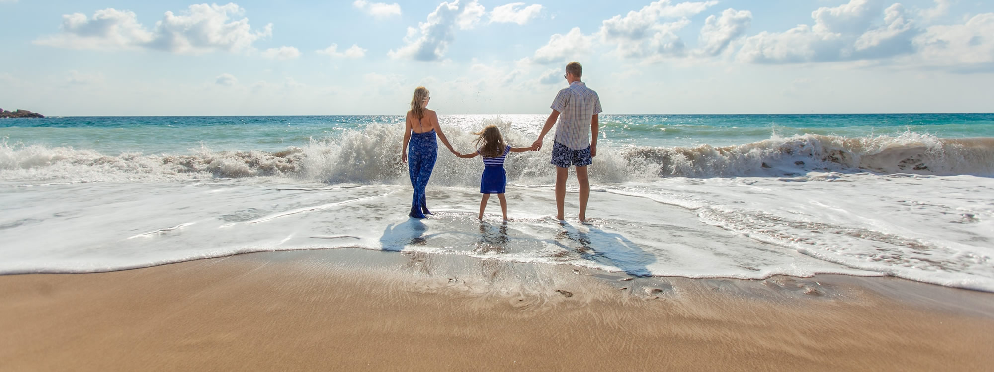 Family holding hands on a beach as waves wash over their feet.