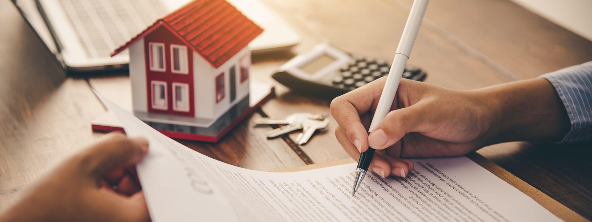 Banner with person signing a contract with a calculator and house keys on the table.